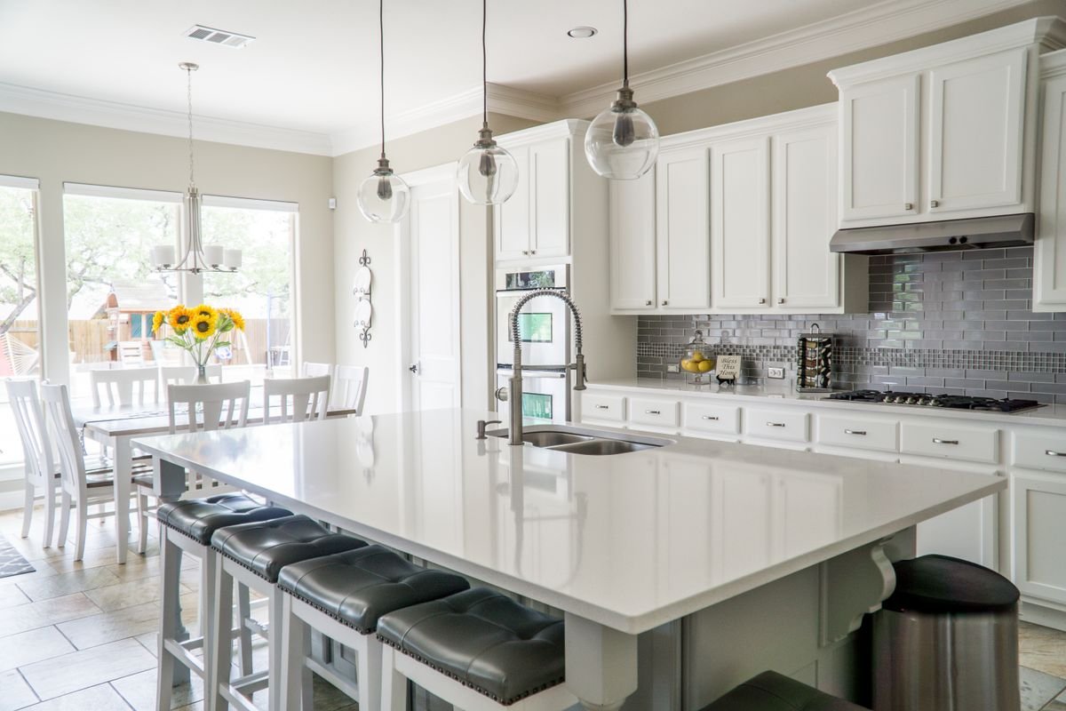Bright kitchen with a large white island countertop, grey subway tile backsplash and beige floor tiles